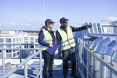 Two Leadec employees inspecting pipes on a factory roof. 
