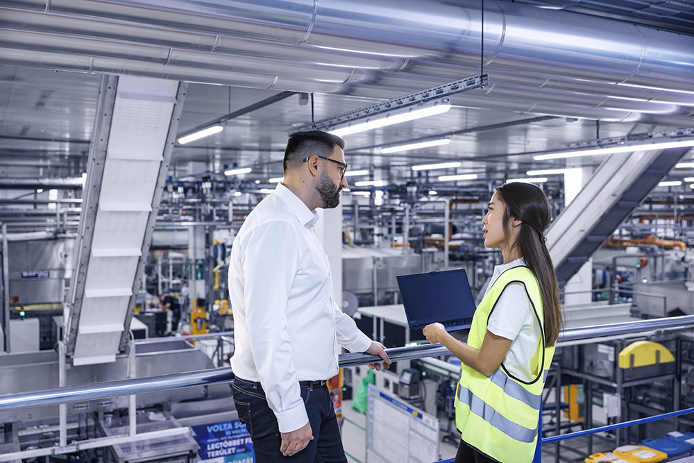 A male and a female Leadec employee with a laptop talking in a production facility.